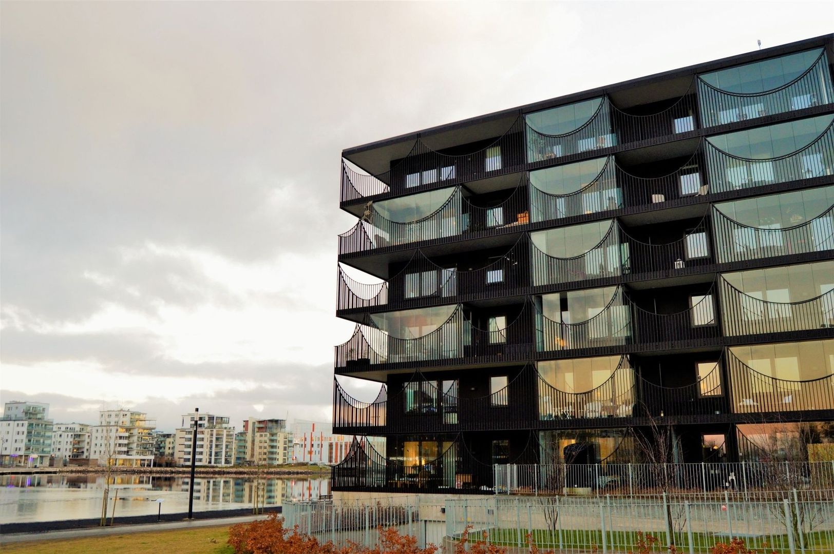 Modernt flerbostadshus med inglasade balkonger vid en stilla kanal